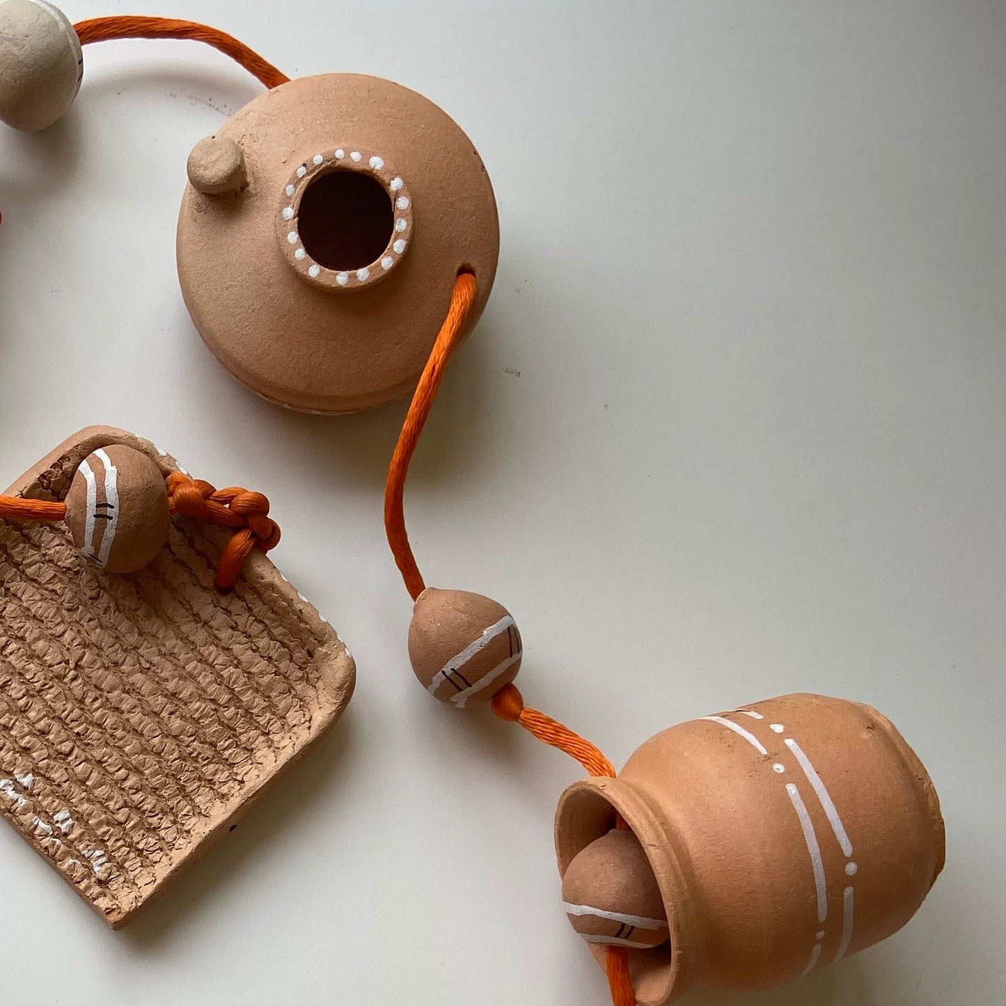 A series of terracotta miniature wall hangings featuring traditional utensils such as an earthern stove, rolling pin, grain grinder, and more, with hand-painted details.