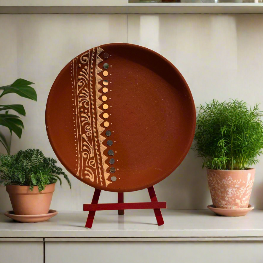 Decorative round clay plate with a pattern on a stand, surrounded by potted plants in a home setting.