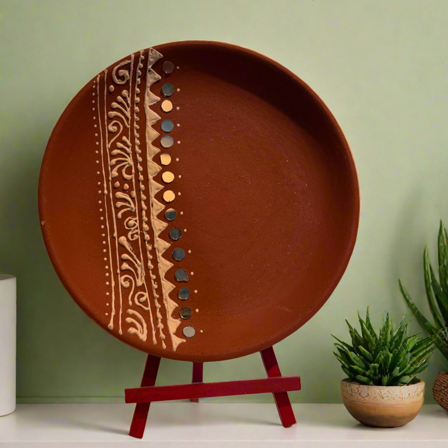Decorative terracotta plate with a pattern on a stand against a green wall.