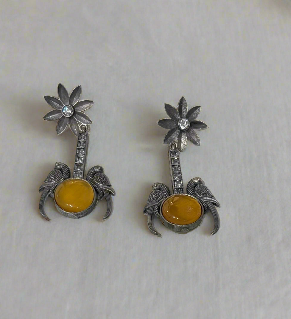 Pair of silver earrings with yellow stones on a light gray background